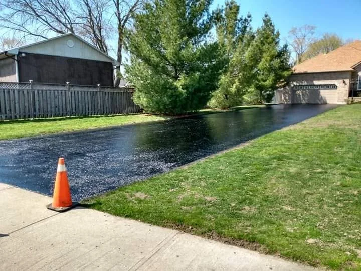 Fresh driveway sealing work by Seal Coat Kings beside grass with a traffic cone.