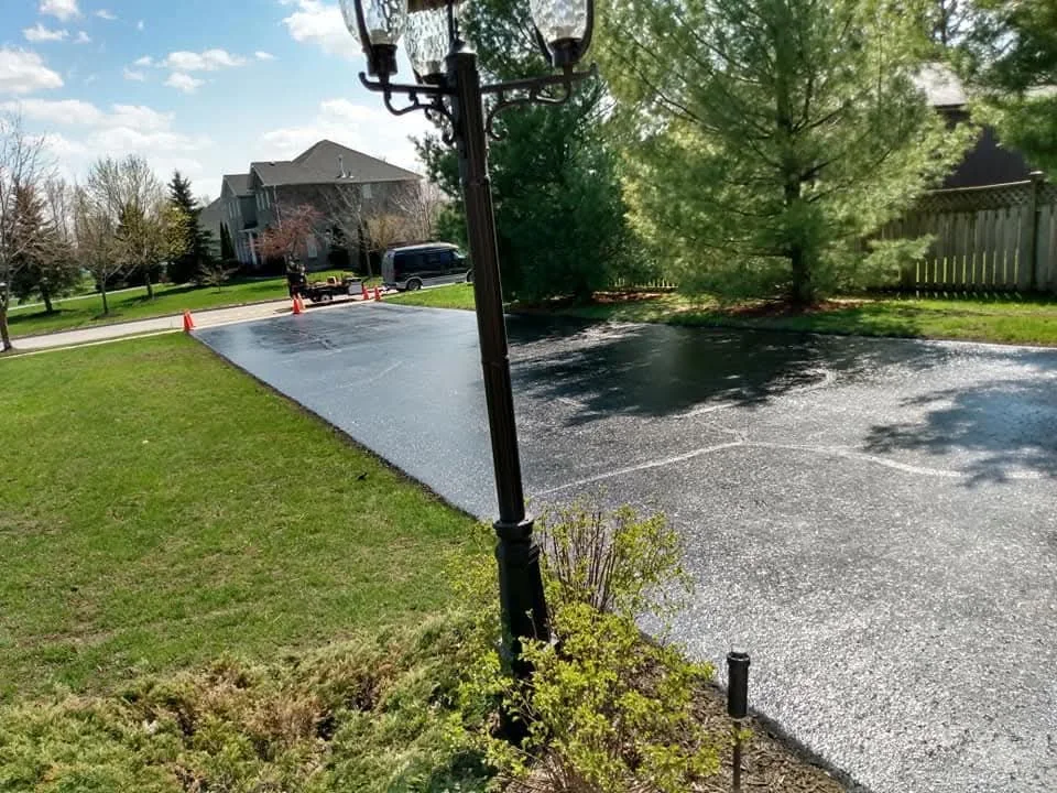 Fresh sealed driveway viewed from a longer distance with lawn and trees.