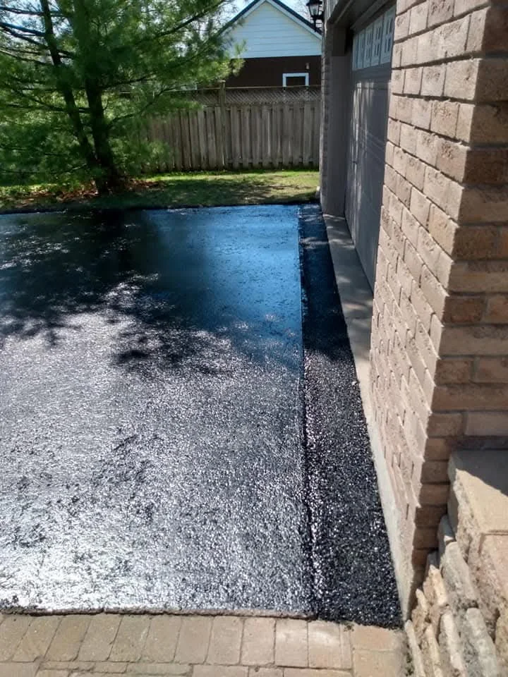 Vertical photo of a freshly sealed driveway beside a house.