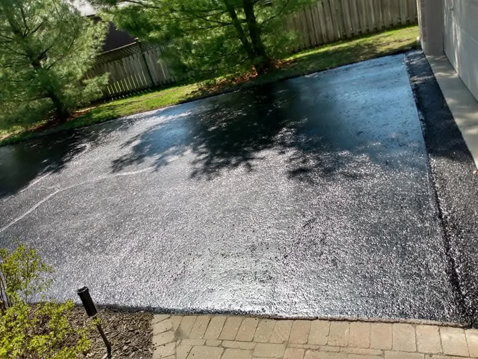 Fresh sealed driveway surface corner beside a fence.